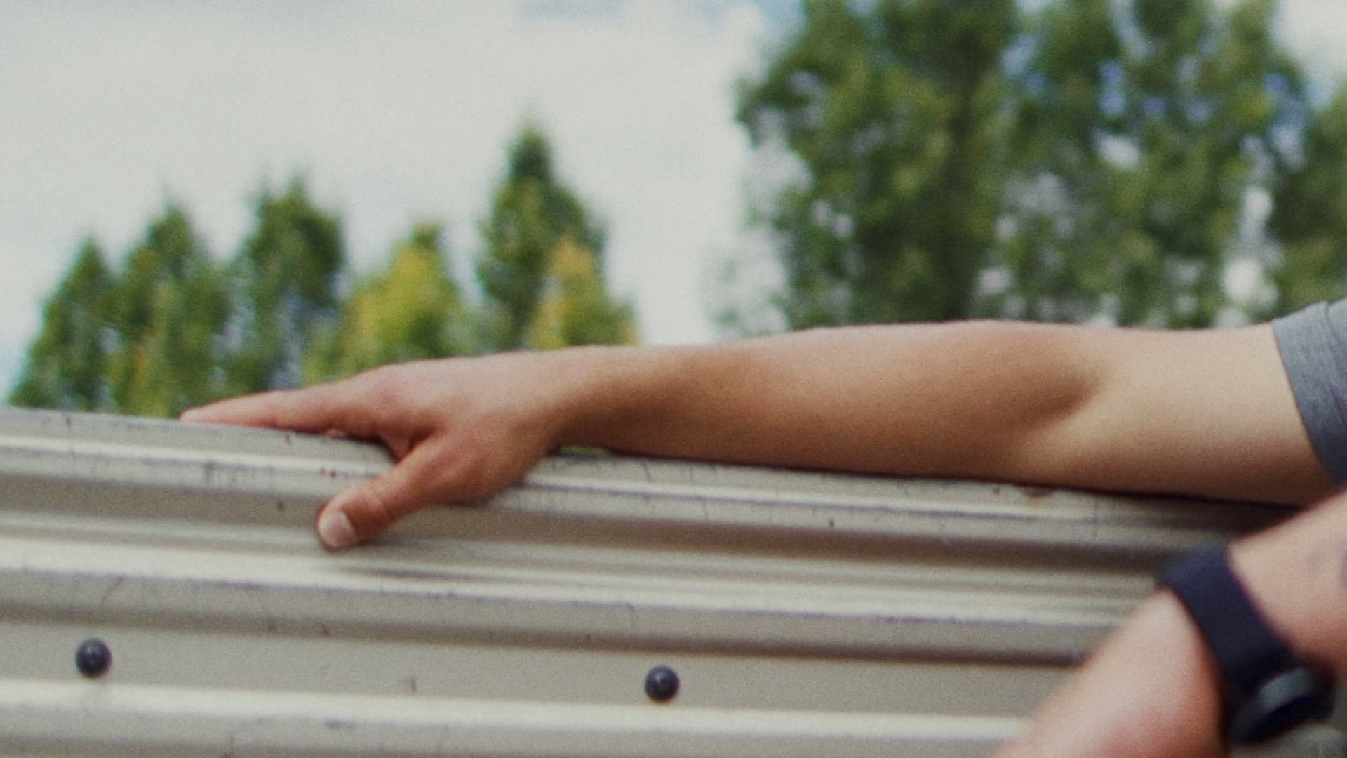 A man resting his arm on a truck bed in the sun, trees behind — a still from the Relay brand film