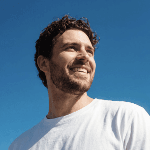 A smiling man with dark curls against a blue sky